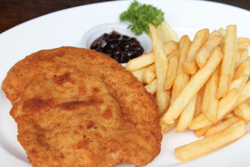 Filled pork schnitzel called Cordon Bleu with French fries, cranberry jam and lemon