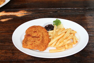 Filled pork schnitzel called Cordon Bleu with French fries, cranberry jam and lemon