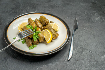 bottom view stuffed grape leaves a fork on white plate and knife on dark background with copy space