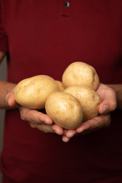 Close up photo of a caucasian man holding potatoes. He is wearing a red t-shirt