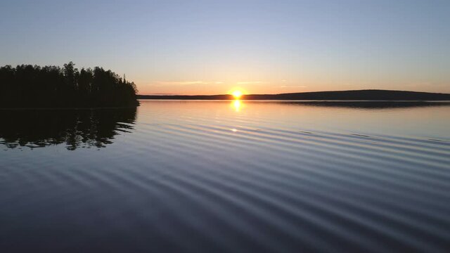 Aerial, drone shot, over the calm, reflecting surface, of lake Posionjarvi, midnight sun, on a sunny, summer evening sunset, midsummer in Posio, Lapland, Finland