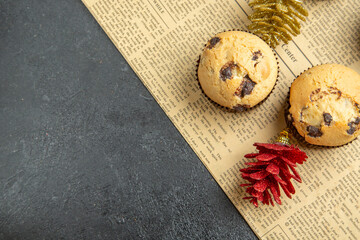 Above view of small cupcakes accessories on newspaper on dark isolated background