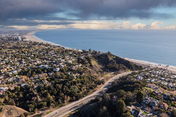 Aerial of Temescal Canyon Road and Pacific Palisades neighborhoods with stormy sky near Santa Monica Bay in Southern California.
