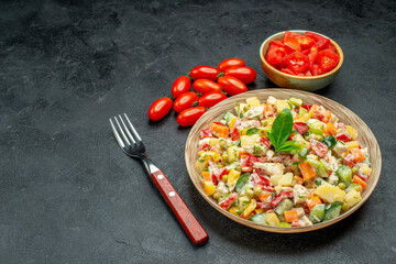 side close view of vegetable salad with tomatoes and fork on side and free place for your text on dark grey background