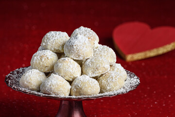 Holiday treat, Russian Teacakes stacked on a red cake plate, on a red velvet tablecloth, red heart for Valentines in the background
