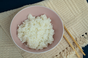 Top view of pink bowl of cooked rice with bamboo hashi