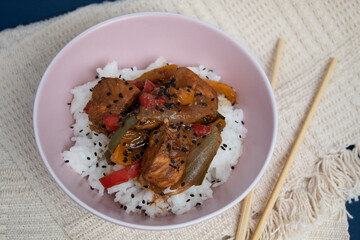 Topview of pink bowl with cooked rice and plaid chicken decorated with black sesame with background
