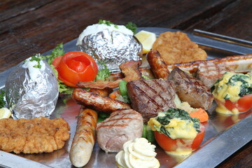Huge mixed grill platter with crumbed pork escalope, beef steaks, pork steaks, German sausages, baked potatoes, herb butter and gratinated tomatoes