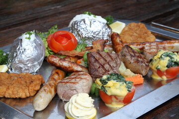 Huge mixed grill platter with crumbed pork escalope, beef steaks, pork steaks, German sausages, baked potatoes, herb butter and gratinated tomatoes