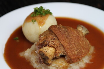 Half Bavarian pork knuckle served on sauerkraut and with potato dumpling on gravy