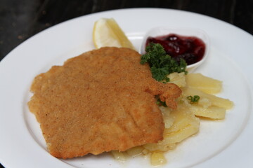 Crumbed pork escalope named Schnitzel, served with potato salad, cranberry jam and lemon