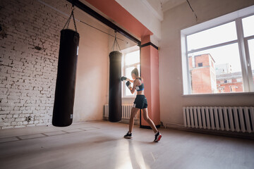 The girl is preparing for a boxing competition and trains punches on a punching bag in a spacious...