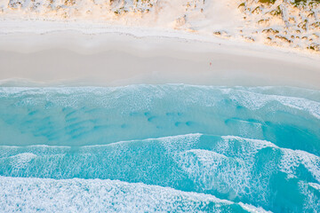 top down view of waves crashing against an empty beach. 