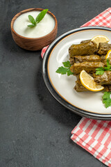 bottom view stuffed grape leaves on white plate a bowl of natural yogurt napkin on dark background with copy space