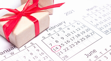 Calendar page with mark valentines day in red circle. 14 February. Handmade gift box wrapped craft paper in the background. Horizontal banner, copy space.