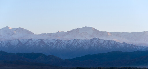 Low contrast photo of mountain range with snow peaks in different shades of blue and cyan. Flat contrast scene with negative space available for text.	