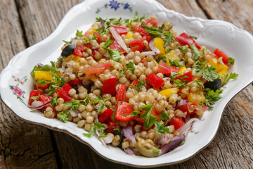 Wheat salad in a bowl. Wheat, peppers, tomatoes, olives, lemon, parsley, olive oil and salt