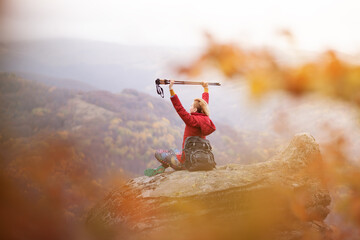 Hiker girl sitting on a rock in the mountains. Enjoying the view with hands up holding hiking...