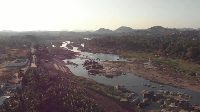 Tungabhadra River flow cascading alongside the rocky landscape Hampi town's edge in Karnataka, India - Aerial Fly-over