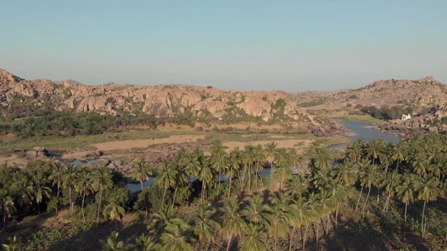 Paradisiac Tungabhadra Riverbank among rocky landscape and lush palm trees in Hampi, Karnataka, India - Aerial panoramic wide shot