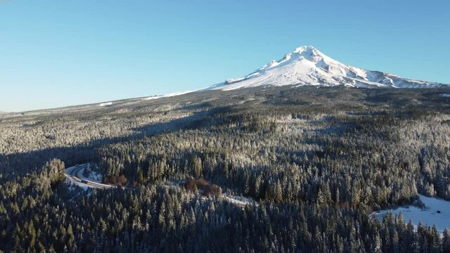 Aerial 4K view of highway weaving through snowy forest near Mount Hood in Oregon. Drone shot of winter landscape in Pacific Northwest panning right.