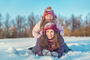Fototapeta na wymiar Little girl and her mother playing outdoors at sunny winter day. Active winter holydays concept.