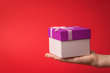 A woman's hand with a gift box on a bright red background.