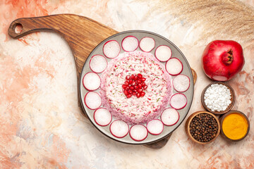 Top view of delicious salad with various ingredients on wooden cutting board and different spices on mixed color background