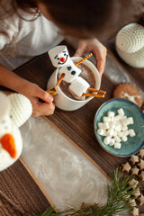 Fototapeta na wymiar Little cute girl plays with knitted snowmen and eats gingerbread and drinks cocoa with marshmallows.