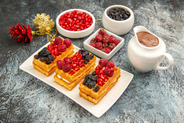 top view waffles with berries on white plate bowls with raspberries raisins pomegranates chocolate red and golden pinecones on grey-white background