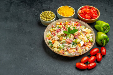 side view of bowl of vegetable salad with different vegetables on side on dark grey background