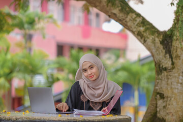 Naklejka premium Photo of beautiful islamic female studentwearing headscarf sitting in park and using silver laptop.