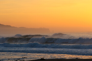 Misty Sunrise on the beach in Japan with large waves breaking onto the sand. It's a stunning scene in a place that is often referred to as the Land of the Rising Sun