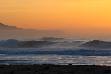 Misty Sunrise on the beach in Japan with large waves breaking onto the sand. It's a stunning scene in a place that is often referred to as the Land of the Rising Sun