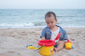 Adorable Cute Asian baby boy playing with beach toys on tropical beach