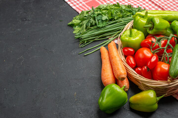 Front view of fresh various organic vegetables in a wooden basket on orange stripped towel on dark background