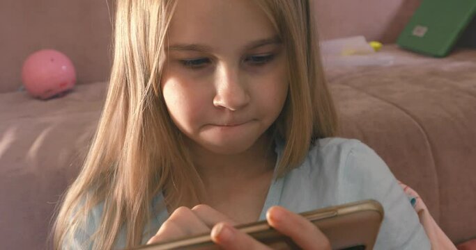 Little girl enjoys playing on smartphone phone in pink room art noise