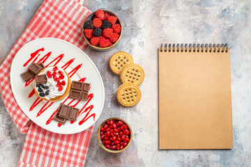top view cake with chocolate on oval plate bowls with pomegranate raspberry candies biscuits kitchen towel a notebook on marble ground