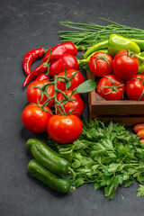 Vertical view of vegetable basket with a bunch of green and peppers cucumber and tomatoes with stem carrots beets on dark background