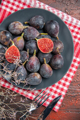 High resolution photo of full fresh black mission figs split ones on a black plate and fork with knives on red stripped towel on colorful table