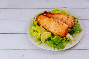 Freshly cooked salmon in plate with salad and lemon on white background.
