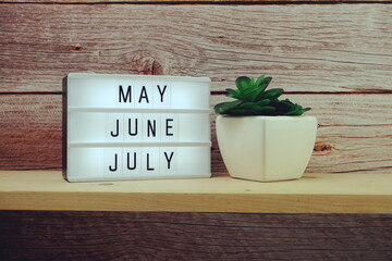 May, June, July word in light box on wooden background