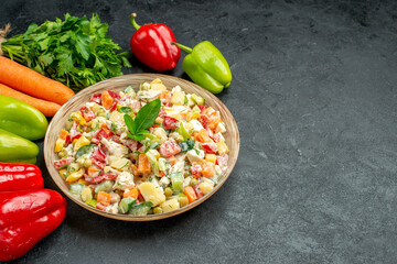 side view of bowl of vegetable salad with carrots greens and bell peppers on side on dark grey table