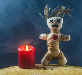 In einer Voodoopuppe stecken Nadeln. Sie steht neben einer brennenden roten Kerze.