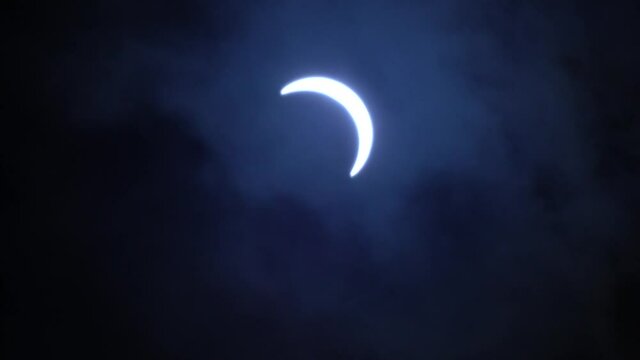 Glowing Partial Solar eclipse crescent, on a cloudy, dark blue sky