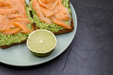 Whole grain bread with avocado paste,lime and salmon. Bruschetta with avocado and trout on a marble surface. Toasted bread with avocado and red fish. The concept is useful and delicious breakfast