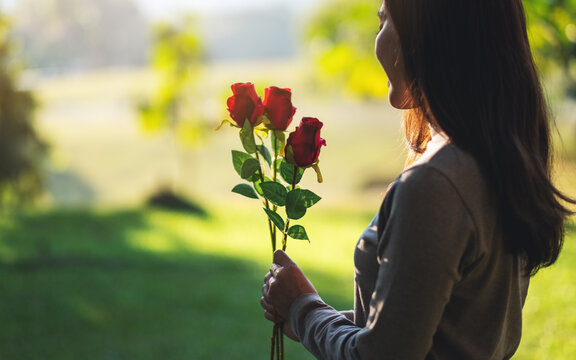 Closeup image of a beautiful asian woman holding red roses flower in the park