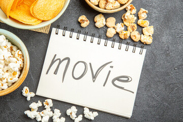 Obraz na płótnie Canvas top view different snacks with movie written notepad on dark background cinema photo junk food