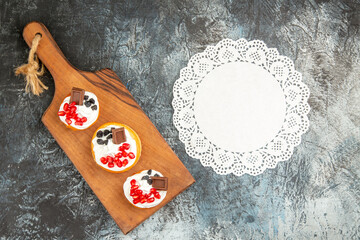 top view berry cakes with chocolate on cutting board white oval lace doily on grey-white background with copy space - obrazy, fototapety, plakaty