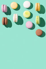 Assorted macaroons on bright blue green colored background, colorful french cookies macarons. Hard light and copy space.